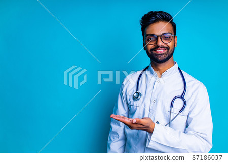 pakistanian doctor in white coat with stethoscope pointing at copyspace with hand mock up over blue studio background pakistanian doctor in white coat with stethoscope pointing at copyspace with hand mock up over blue studio background 87186037