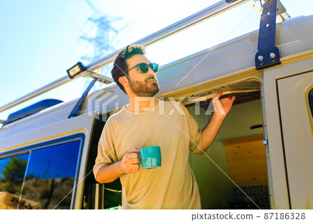 man in charming trailer house makes coffee outdoors in mountains in summer sunny day 87186328