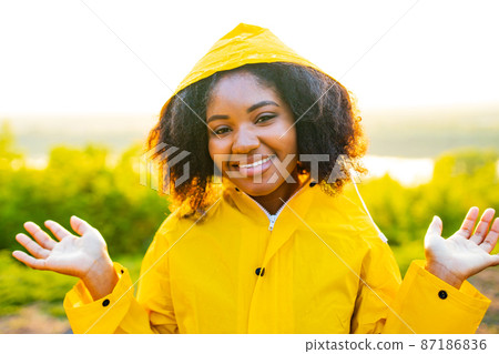 afro amrican woman curly hair wear yellow raincoat and looking at camera outdoor sunset lights afro amrican woman curly hair wear yellow raincoat and looking at camera outdoor sunset lights 87186836