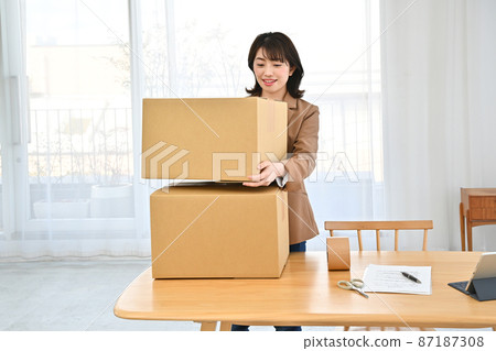 A woman who lifts two cardboard boxes on a desk 87187308