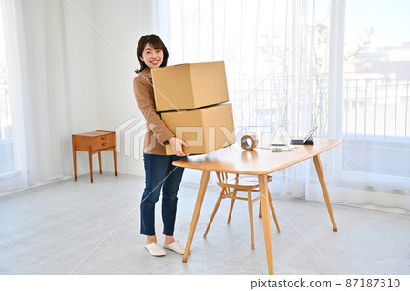 A woman who lifts two cardboard boxes on a desk 87187310