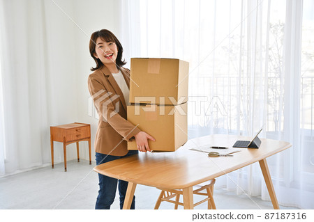 A woman who lifts two cardboard boxes on a desk A woman who lifts two cardboard boxes on a desk 87187316