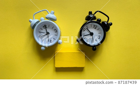 White and black alarm clock on yellow background with small wooden. Copy space White and black alarm clock on yellow background with small wooden. Copy space 87187439