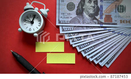 Top view of alarm clock, bank notes and pen on red background. Copy space Top view of alarm clock, bank notes and pen on red background. Copy space 87187453