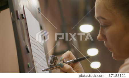 Woman artist learns to paint with airbrush with acrylic dye, paper and easel. Concept modern art, airbrushing, aerography, graffiti, aerosol spray 87188121