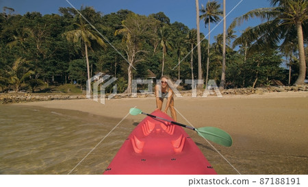 Woman pulls canoe with paddle to azure sea water from beach 87188191