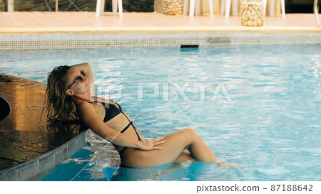 The pretty woman drinking blue cocktail alcohol liquor and sit at the bar. Cocktail bar in the swimming pool. Portrait of sexy girl in pool outdoor. 87188642