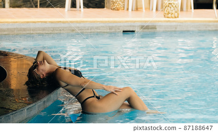 The pretty woman drinking blue cocktail alcohol liquor and sit at the bar. Cocktail bar in the swimming pool. Portrait of sexy girl in pool outdoor. The pretty woman drinking blue cocktail alcohol liquor and sit at the bar. Cocktail bar in the swimming pool. Portrait of sexy girl in pool outdoor. 87188647