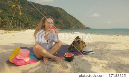 The cheerful woman in holding and eating slices of watermelon on tropical sand beach sea. Portrait attractive girl spend summer weekend. The cheerful woman in holding and eating slices of watermelon on tropical sand beach sea. Portrait attractive girl spend summer weekend. 87188815