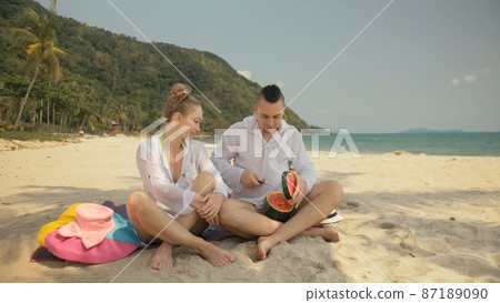 The cheerful love couple holding and eating slices of watermelon on tropical sand beach sea. Romantic lovers two people spend summer weekend. The cheerful love couple holding and eating slices of watermelon on tropical sand beach sea. Romantic lovers two people spend summer weekend. 87189090