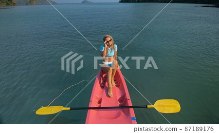 Pretty slim woman in elegant swimsuit lies in pink plastic kayak drifting on azure ocean at exotic resort upper view. Pretty slim woman in elegant swimsuit lies in pink plastic kayak drifting on azure ocean at exotic resort upper view. 87189176