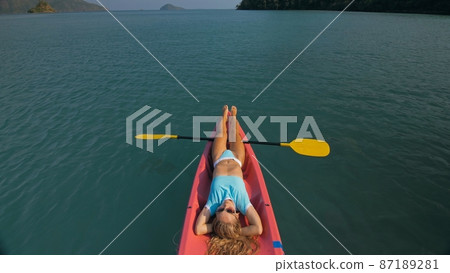 Pretty slim woman in elegant swimsuit lies in pink plastic kayak drifting on azure ocean at exotic resort upper view. Pretty slim woman in elegant swimsuit lies in pink plastic kayak drifting on azure ocean at exotic resort upper view. 87189281