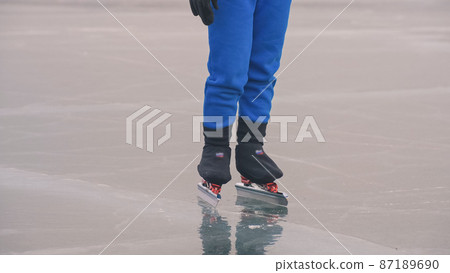 The child train on ice speed skating. The legs in skates close up. The kid girl skates in the winter in sportswear sport glasses. Outdoor slow motion. 87189690
