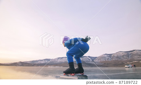 The child train on ice speed skating. The athlete at the start, in a sports stance. The kid girl skates in the winter in sportswear, sport glasses. 87189722