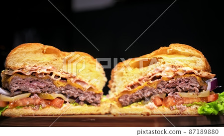 Cut craft burger is cooking on black background. Consist: sauce, lettuce, tomato, red onion, pickle, cheese, bacon, air bun and marbled meat beef. Cut craft burger is cooking on black background. Consist: sauce, lettuce, tomato, red onion, pickle, cheese, bacon, air bun and marbled meat beef. 87189880