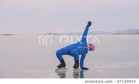 The child train on ice speed skating. The athlete stretches, warms up, rest. The kid girl skates in sportswear, sport glasses. Outdoor slow motion. 87189954
