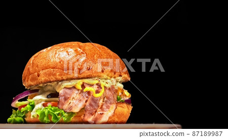Craft burger is cooking on black background. Consist: sauce, lettuce, tomato, red onion, cucumber, cheese, bacon, air bun and breast of chicken. Craft burger is cooking on black background. Consist: sauce, lettuce, tomato, red onion, cucumber, cheese, bacon, air bun and breast of chicken. 87189987