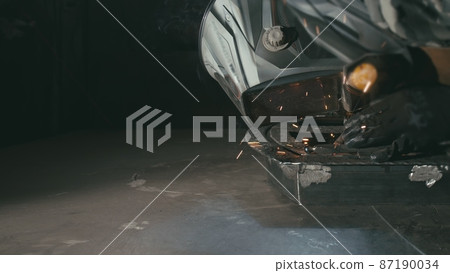 Forge workshop. Smithy. Worker in a welding hood helmet welds a part by electric welding. Sparks are reflected in the protective screen. Forge workshop. Smithy. Worker in a welding hood helmet welds a part by electric welding. Sparks are reflected in the protective screen. 87190034