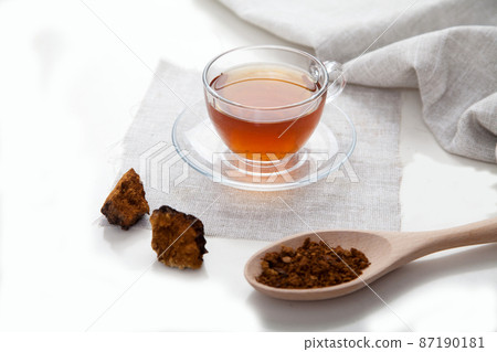 Chaga coffee in a glass cup, pieces of chaga and a linen salyette on a light background. Health concept. 87190181