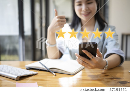Smiling young woman using smart phone and showing thumb up with gold five star icon for to review the service. Smiling young woman using smart phone and showing thumb up with gold five star icon for to review the service. 87191551