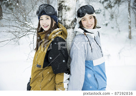 Snowboarding girls posing at a snowy ski resort Snowboarding girls posing at a snowy ski resort 87192816