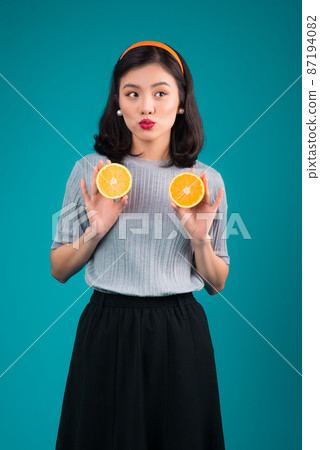 Healthy food. Smiling lovely pinup asian girl holding orange over blue background. Healthy food. Smiling lovely pinup asian girl holding orange over blue background. 87194082