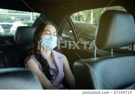 Beautiful Asian businesswoman wear a hygiene protective face mask taking a back seat in taxi portrait, happy Asian woman passenger with face mask traveling by using taxi during the COVID-19 pandemic. 87194714