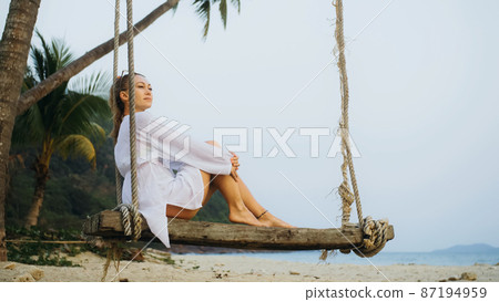 Woman on the swing on tropical beach. The girl in white shirt en Woman on the swing on tropical beach. The girl in white shirt en 87194959