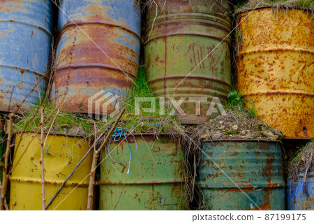 Colorful stacked barrels behind deciduous apple trees with fallen leaves and fallen yellow apples in a field 87199175