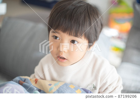 一個 4 歲的男孩在陽光明媚的家庭公寓的客廳裡一邊打被爐一邊說話 87199206