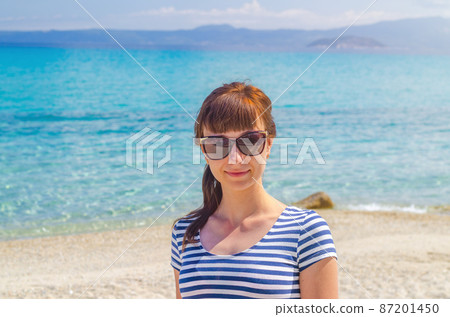 Close-up portrait of young beautiful girl with striped t-shirt and sunglasses looking at camera and smile 87201450