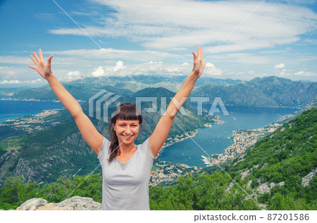 Young beautiful girl traveler with grey t-shirt raise hands and smile on top of mountain Young beautiful girl traveler with grey t-shirt raise hands and smile on top of mountain 87201586