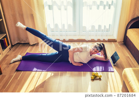 Young attractive woman in sports clothing doing workout at home 87201684