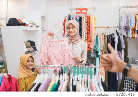 muslim mother choosing shirt with daughter during shopping at fashion shop 87203419