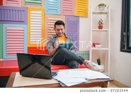 Handsome man smiling while writing and working using laptop 87203544