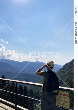 Man with a hat looks binoculars into the distance. Mountain landscape. Mobile photo Man with a hat looks binoculars into the distance. Mountain landscape. Mobile photo 87204460