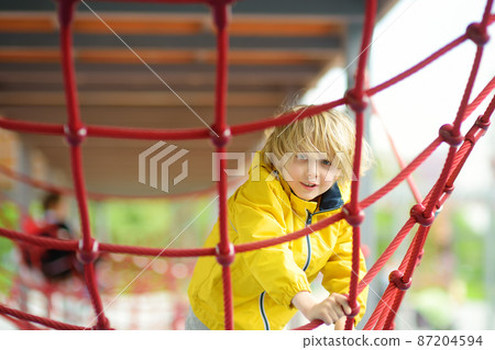 Cute preschooler boy having fun on outdoor playground. Spring summer autumn active sport leisure for kids. Activity for family with children. Equipment of entertainment park Cute preschooler boy having fun on outdoor playground. Spring summer autumn active sport leisure for kids. Activity for family with children. Equipment of entertainment park 87204594