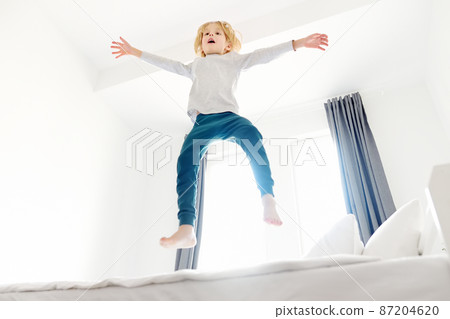 Happy little boy in pajamas jumps on his parents bed in the morning. A happy childhood for kids with a loving family. Happy little boy in pajamas jumps on his parents bed in the morning. A happy childhood for kids with a loving family. 87204620