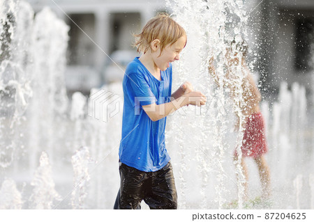 Little boy plays in the square between the water jets in the dry fountain at sunny summer day. Active leisure for kids in the city. 87204625