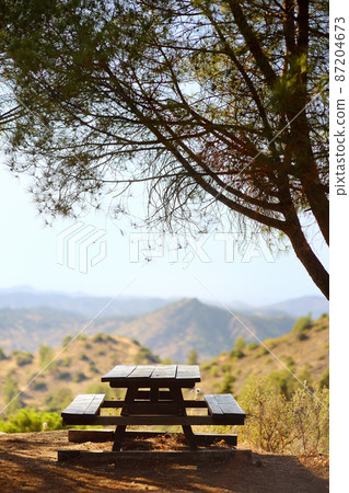 Wooden picnic table with view of picturesque landscape in the Troodos mountains on a sunny summer day. National park "Troodos Mountains", Cyprus. Wooden picnic table with view of picturesque landscape in the Troodos mountains on a sunny summer day. National park "Troodos Mountains", Cyprus. 87204673