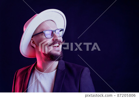 Handsome stylish beard man in white wide-brimmed hat in blazer in glasses is smiling. color filters Handsome stylish beard man in white wide-brimmed hat in blazer in glasses is smiling. color filters 87205806