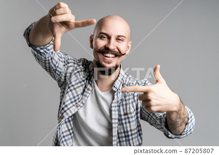 creative bald bearded photographer making frame with fingers in front of face over gray background creative bald bearded photographer making frame with fingers in front of face over gray background 87205807