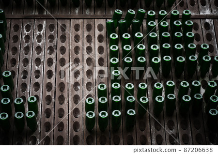 Bottles of wine are stored in wooden shelves with holes. 87206638