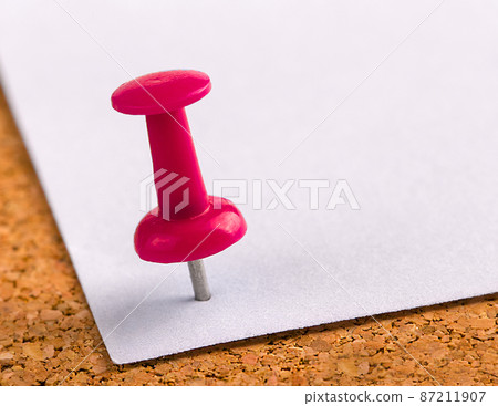 plastic button with a needle stuck in an iron sheet of white paper on a wooden stopper 87211907