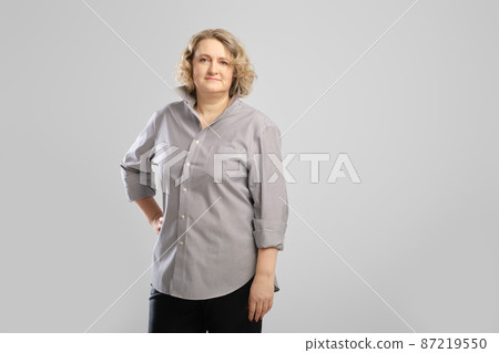Casual portrait of senior woman in grey shirt and trousers over grey studio background 87219550