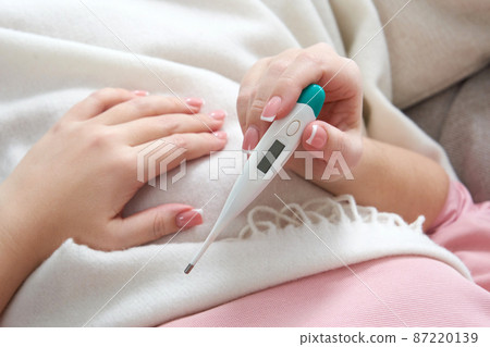 Woman holding a digital thermometer. Concept of fever, flue, virus and quarantine Woman holding a digital thermometer. Concept of fever, flue, virus and quarantine 87220139