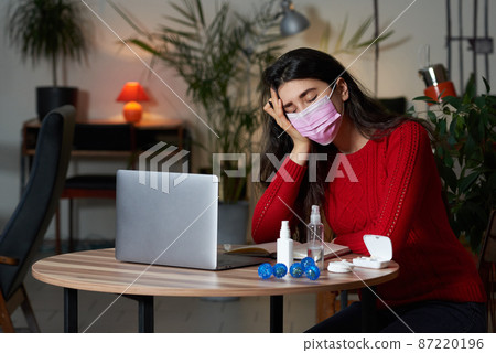 sick woman with pills and thermometer on a table working on a laptop from home on quarantine isolation. 87220196