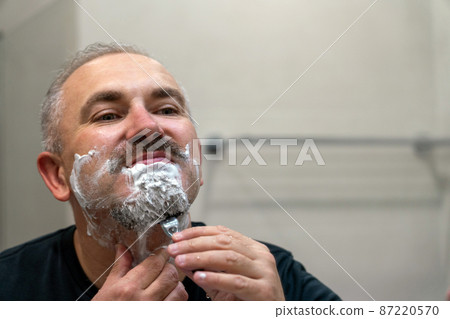 Middle aged handsome man shaving his beard in bathroom 87220570