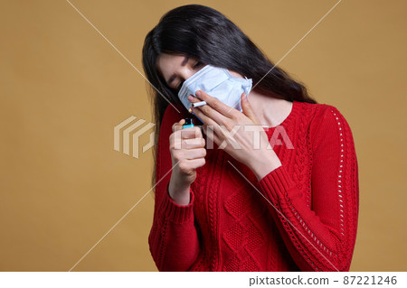Young girl wearing medical protective mask lights up, holding a cigarette in her mouth through the mask Young girl wearing medical protective mask lights up, holding a cigarette in her mouth through the mask 87221246