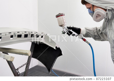 Mechanic painting bumper of a car with sprayer in painting booth in repair auto service 87223107